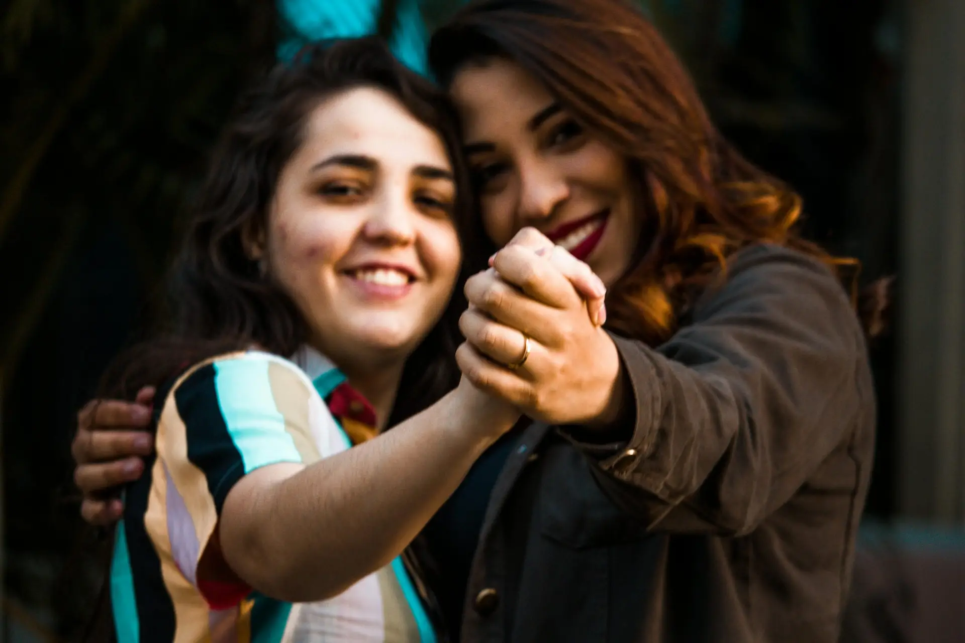 Two happy women holding hands and smiling warmly, outdoors setting.
