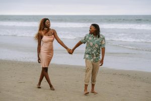 A loving black lesbian couple holding hands and walking on a serene beach.
