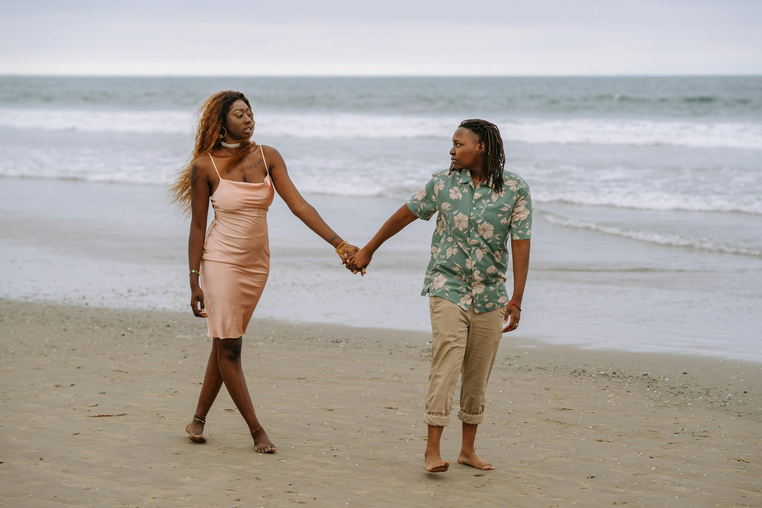 A loving black lesbian couple holding hands and walking on a serene beach.